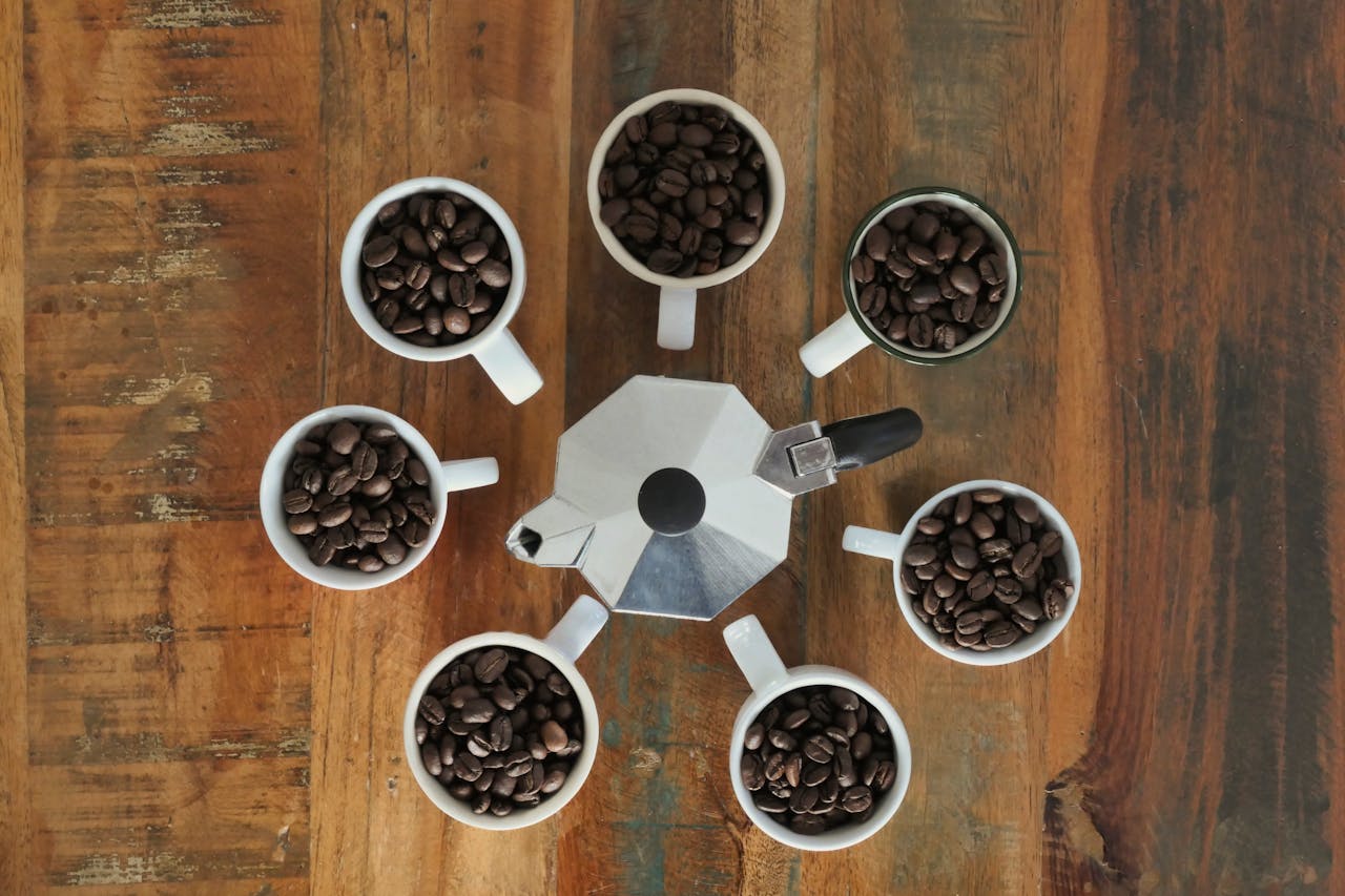 Aromatic coffee beans in cups around a classic moka pot on a rustic wooden table.